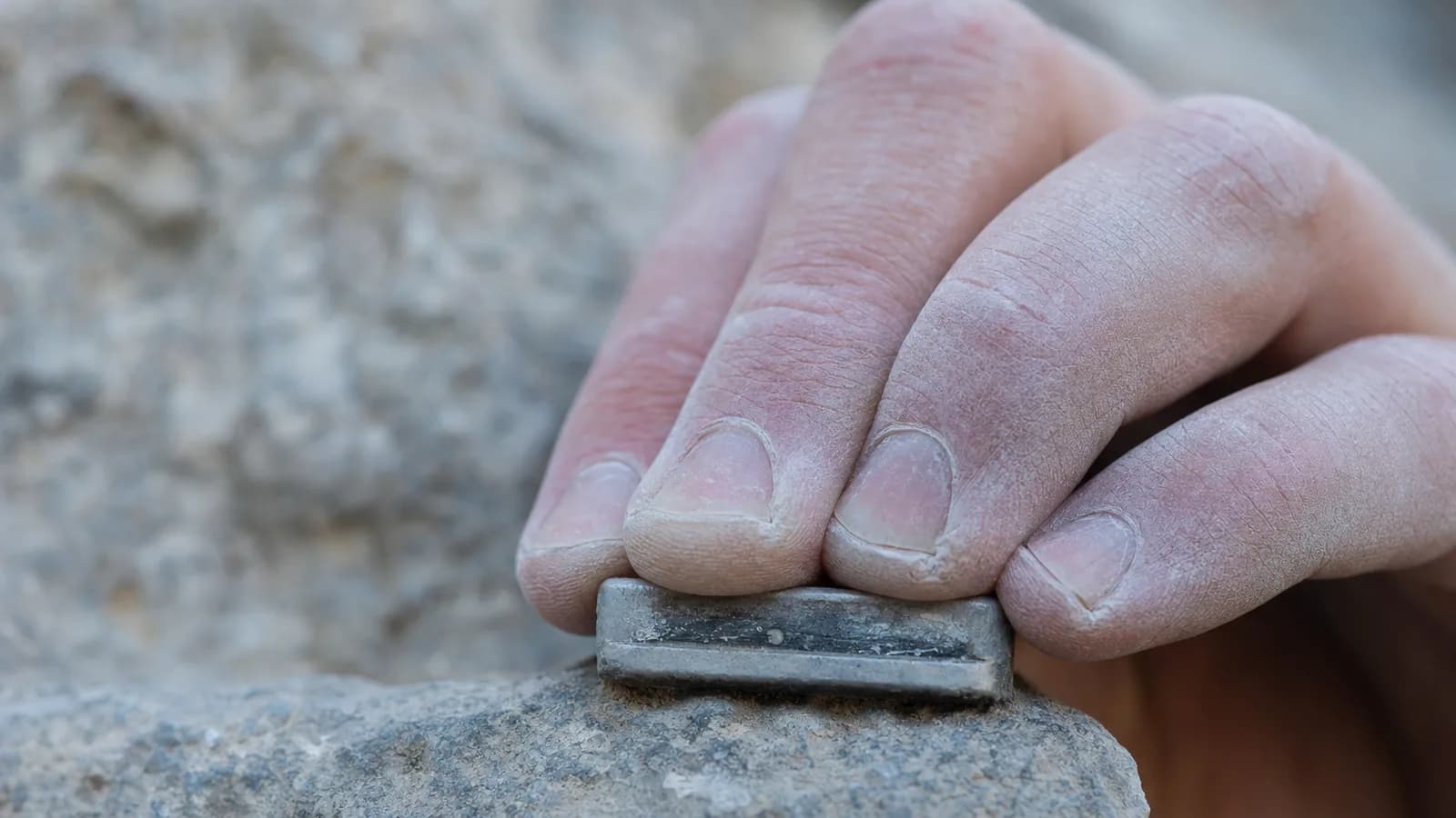 Plan rapproché de quatre doigts en demi arquée sur une réglette calcaire grise de 1 cm, magnésie blanche aux doigts, tendons saillants sur le dos de la main